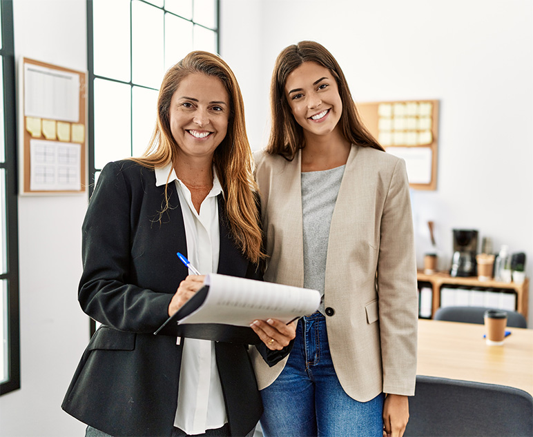 Two smiling women standing side by side in an office