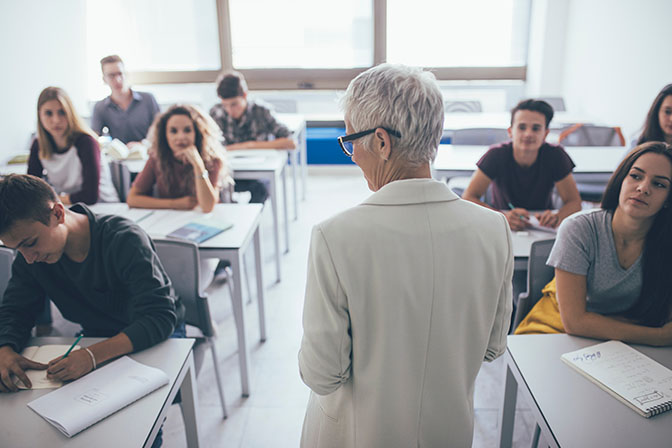 woman teacher standing at classroom and talking to high school students.